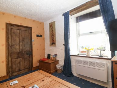 A room with a wooden door a window with blue curtains a wooden chest and a table with coasters at Bod Feurig in Penygroes