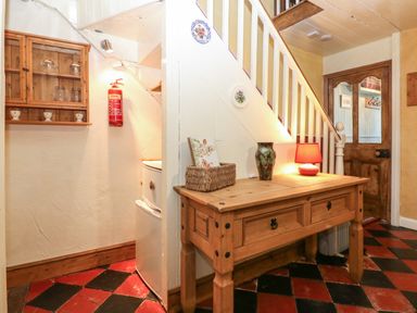 A hallway with a wooden table with a lamp and vase under stairs with a wooden cabinet and fire extinguisher on the wall at Bod Feurig Penygroes