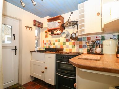 A kitchen with a stove a sink wooden countertops and colorful tiled backsplash at Bod Feurig in Penygroes