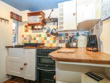 A kitchen with a sink oven wooden countertop hanging pots and multicolored tiled backsplash at Bod Feurig in Penygroes