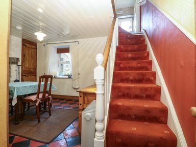 A staircase with red carpet beside a dining area with a table and wooden chairs at Bod Feurig in Penygroes
