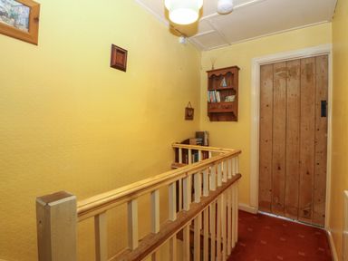 A hallway with wooden railing yellow walls a wooden door and shelves with books at Bod Feurig Penygroes