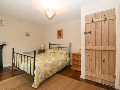 A bedroom with a metal bed frame and floral bedding two wooden bedside tables with lamps a wooden door and wooden flooring at Bod Feurig in Penygroes