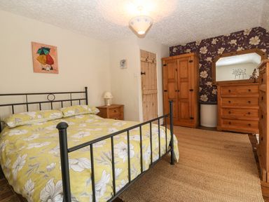A bedroom with a metal bed frame with floral bedding a wooden wardrobe dresser and mirror at Bod Feurig in Penygroes