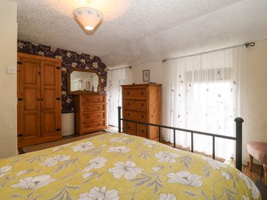 A bedroom with a bed in the foreground wooden wardrobe dressers mirror and sheer curtains at Bod Feurig in Penygroes