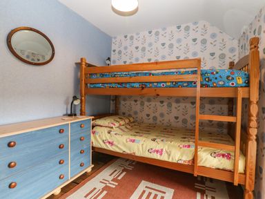 A bedroom with a wooden bunk bed a blue chest of drawers and a wall mirror at Bod Feurig in Penygroes