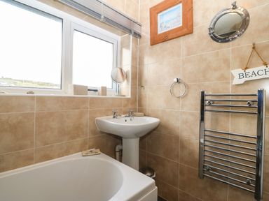 A bathroom with a bathtub sink towel rack window and wall decorations at Bod Feurig in Penygroes