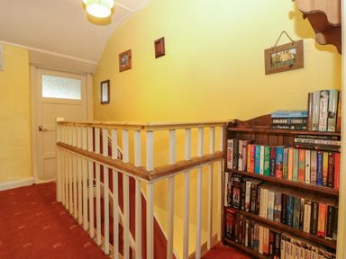 A hallway with yellow walls a white door a wooden handrail and a bookshelf filled with books at Bod Feurig in Penygroes