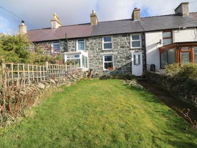 A row of stone terraced houses with a grass lawn and a pathway leading to a white door at Bod Feurig in Penygroes