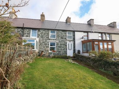 A stone house with white doors and windows and a green lawn in front at Bod Feurig in Penygroes
