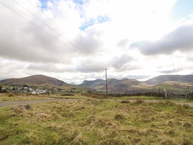 A rural landscape with a grassy field a gravel road a stone wall and houses at the base of hills at Bod Feurig in Penygroes
