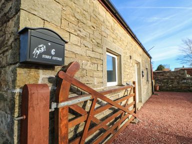 A stone exterior wall with a black mailbox numbered 6 and a wooden gate at Stable Cottage in Hallbankgate
