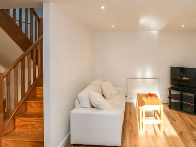 A living room with a white sofa and a wooden coffee table with fruit bowl next to a staircase and a television on a stand at Stable Cottage in Hallbankgate