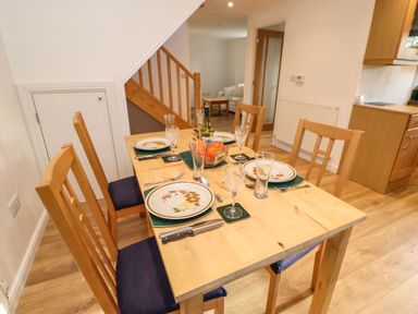 A dining table set with plates glasses cutlery and a bowl of fruit in a dining area at Stable Cottage in Hallbankgate
