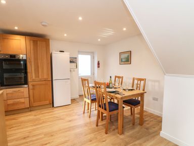 A dining area with a wooden table set for four near a white refrigerator and wooden kitchen cabinets at Stable Cottage in Hallbankgate