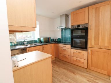 A kitchen with wooden cabinets a double oven teal appliances and a sink under a window at Stable Cottage in Hallbankgate