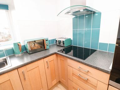 A kitchen countertop with a kettle microwave toaster and electric stove with wooden cabinets at Stable Cottage in Hallbankgate