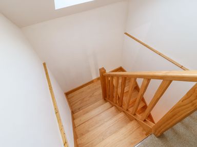 A wooden staircase with a wooden banister and white walls at Stable Cottage in Hallbankgate