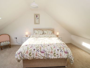 A bedroom with a double bed with floral bedding two bedside tables with lamps and a chair at Stable Cottage in Hallbankgate