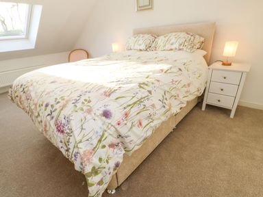 A bedroom with a bed covered in floral bedding a bedside table with a lamp and a window at Stable Cottage in Hallbankgate