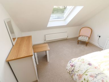 A bedroom with a white dresser a small table a chair a skylight window and a bed with floral bedding at Stable Cottage in Hallbankgate