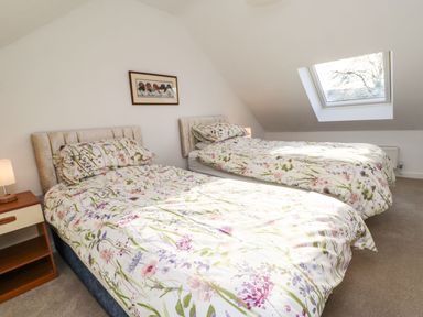 A bedroom with two single beds with floral bedding a bedside table with a lamp a skylight window and a picture on the wall at Stable Cottage in Hallbankgate