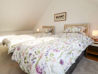 A bedroom with two beds with floral bedding a nightstand with lamp and a framed picture on the wall at Stable Cottage in Hallbankgate