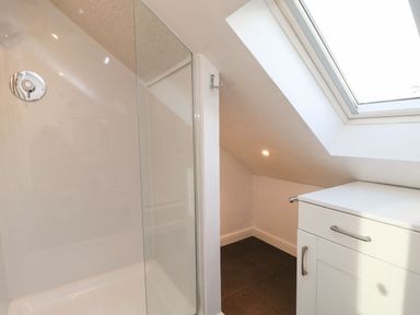 A bathroom shower area with glass door a white cabinet under a skylight at Stable Cottage in Hallbankgate