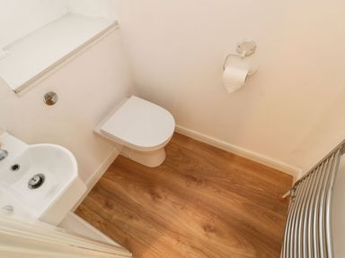 A small bathroom with a white toilet a white sink a toilet paper holder and a metal towel rail on wooden floor at Stable Cottage in Hallbankgate