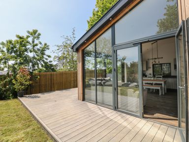 A wooden deck outside a house with glass doors leading to a living area with a dining table and chairs at The Nest Brython in Tenby
