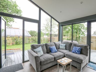 A sitting area with a gray L-shaped sofa and small wooden table in a room with large glass windows and doors at The Nest Brython in Tenby