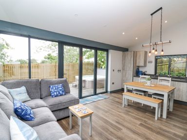 An open plan living room and kitchen with a grey sofa and wooden dining table at The Nest Brython in Tenby