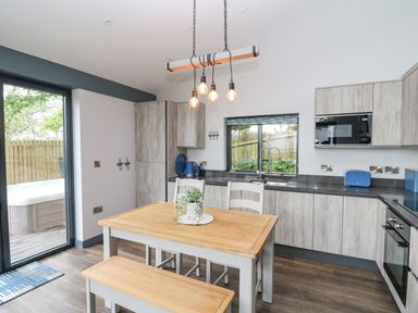 A kitchen with wooden dining table and bench with hanging light bulbs and sliding door at The Nest Brython in Tenby