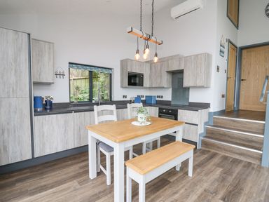 A kitchen with wooden cabinets a dining table with chairs and bench and stairs leading to wooden doors at The Nest Brython in Tenby