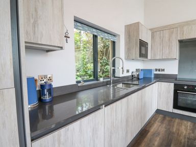 A kitchen with wood cabinets a black countertop a sink a window and blue kitchen appliances at The Nest Brython in Tenby