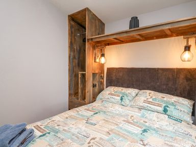 A bedroom with a bed covered in patterned bedding with sea-themed designs and a wooden wardrobe with hanging lights at The Nest Brython in Tenby