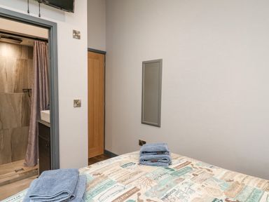 A bedroom with a bed covered in printed bedding and folded towels with a door and bathroom visible at The Nest Brython in Tenby
