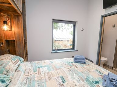 A bedroom with a bed covered in a printed bedspread with folded towels on top a window and a doorway to a bathroom at The Nest Brython in Tenby