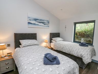 A bedroom with two single beds, nightstands with lamps, and a window showing greenery at The Nest Brython in Tenby