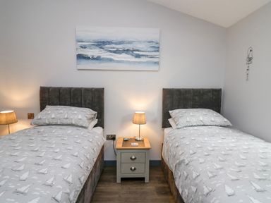 A bedroom with two single beds a nightstand between them and a painting above at The Nest Brython in Tenby