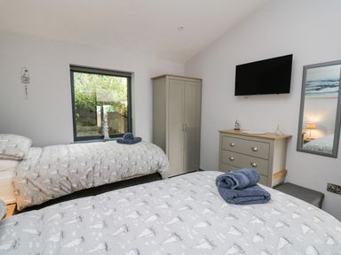 A bedroom with two single beds a wardrobe a chest of drawers and a wall-mounted television at The Nest Brython in Tenby