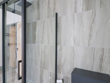 A bathroom with glass shower door gray tiled walls black fixtures and a black cabinet at The Nest Brython in Tenby