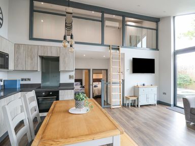 A kitchen and dining area with wooden table and chairs loft ladder and wall mounted tv at Cornerstones Brython in Tenby