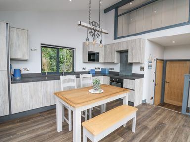 A kitchen with wooden table bench and chairs wooden cabinets and window at Cornerstones Brython in Tenby