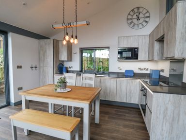 A kitchen with wooden cabinets a dining table and bench and a window above the sink at Cornerstones Brython in Tenby