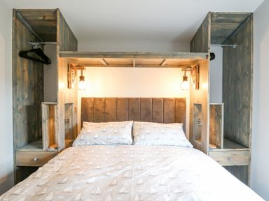 A bedroom with a bed with patterned bedding and wooden shelving on both sides at Cornerstones Brython in Tenby