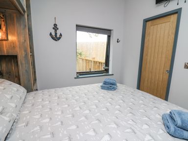 A bedroom with a bed covered in sailboat patterned bedding a wooden door and a window with blue-trimmed sill at Cornerstones Brython in Tenby