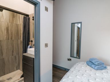 A bedroom with a bed and towels next to a bathroom with a shower at Cornerstones Brython in Tenby