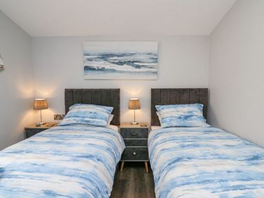 A bedroom with two single beds with blue patterned bedding and a nightstand with a lamp between them at Cornerstones Brython in Tenby