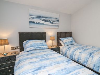A bedroom with two single beds with blue and white bedding bedside tables and lamps at Cornerstones Brython in Tenby